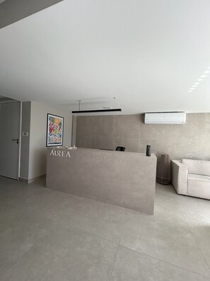 A reception desk with a sign reading "AUREA" in a modern, minimalist lobby with a tiled floor and a sofa in the background. - Flat Cabo Branco Aurea 50m do mar 105 (Joao Pessoa)