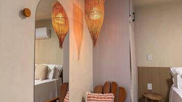 A room with a bed, a wooden chair, a small wooden stool, and two hanging lamps.