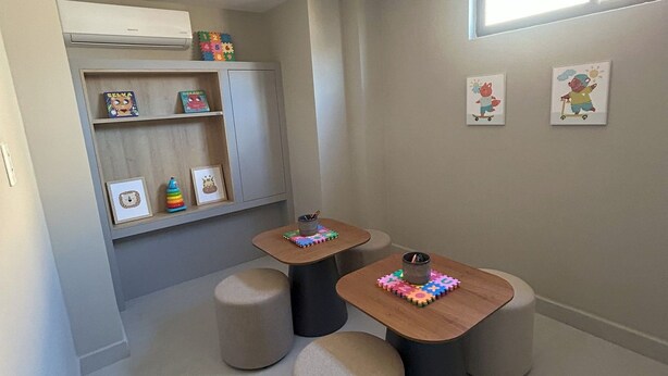 Ein kinderfreundliches Zimmer mit Spielbereich, darunter ein Regal mit Spielzeug und Büchern, sowie zwei kleine Tische mit Hocker.
