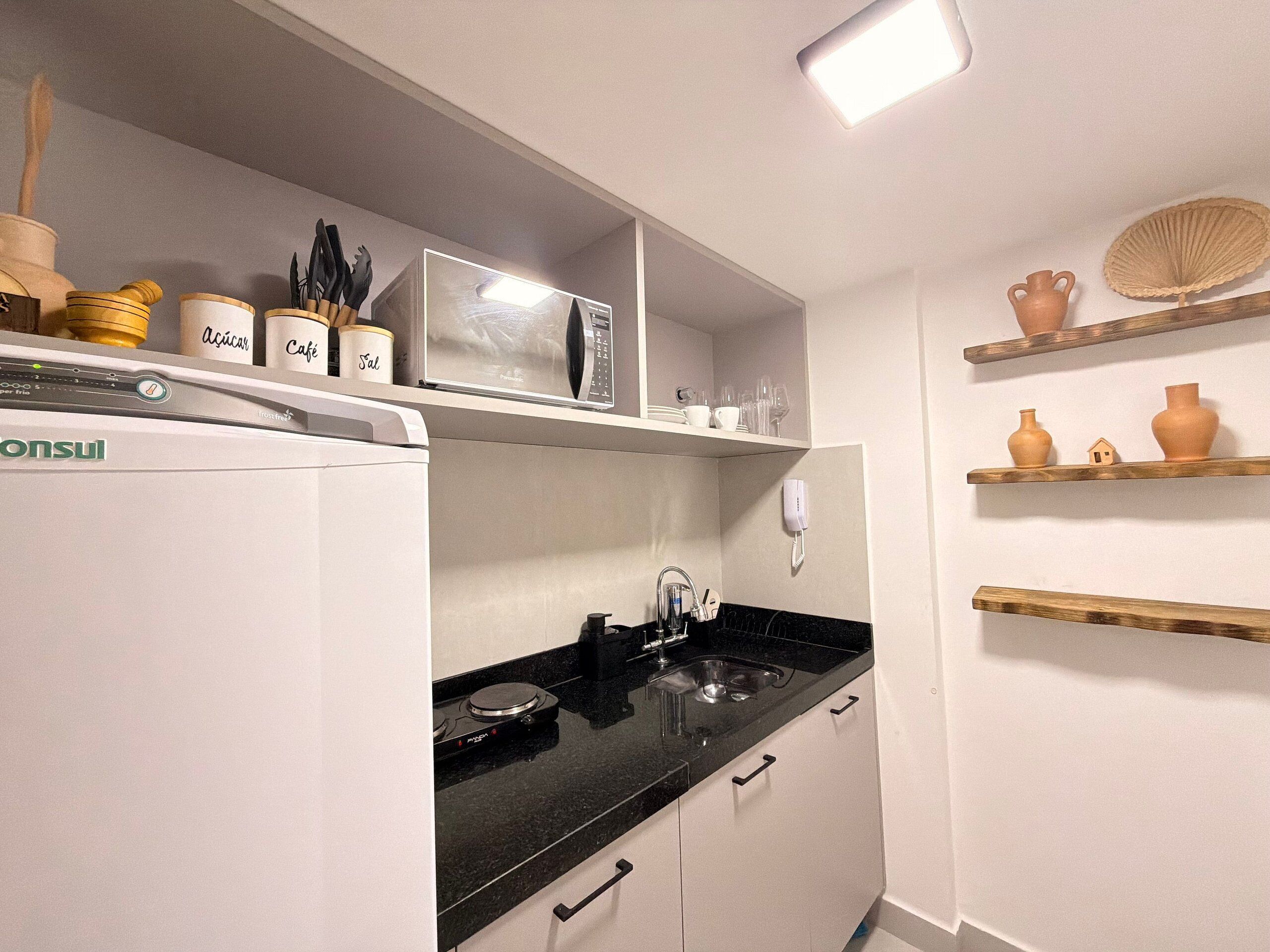 A kitchen with a refrigerator, microwave, sink, and shelves with kitchenware.