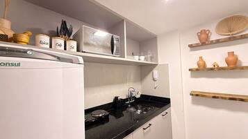 A kitchen with a refrigerator, microwave, sink, and shelves with kitchenware.
