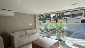 Ein modernes Wohnzimmer mit einem beigen Sofa, einem braunen Ottomanen und einem Glastisch.