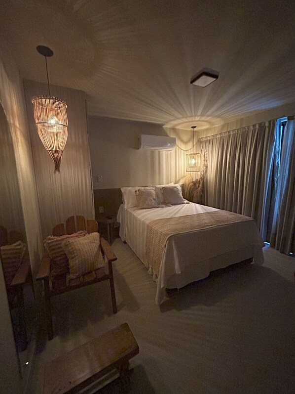 A spacious bedroom with a large bed, a hanging light fixture, a bedside table, and a chair.