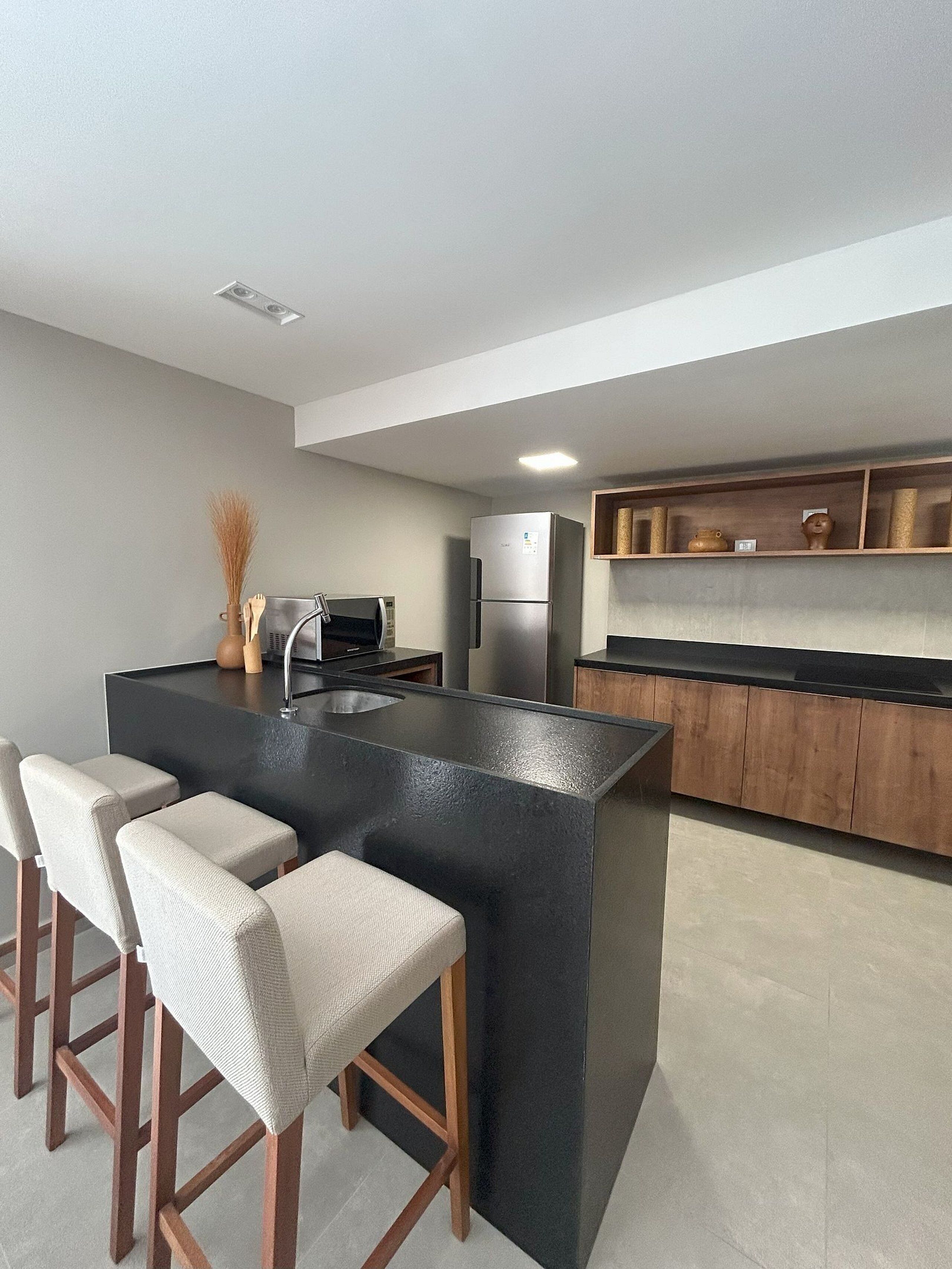 Una cocina moderna con una isla central, taburetes de bar, microondas y refrigerador.