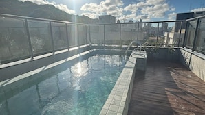 Ein Pool auf dem Dach mit klarem Wasser, umgeben von einer Holzterrasse und einem Glasgeländer.