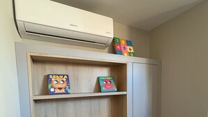 A corner of a room with a wooden shelf unit containing children's books and toys. - Flat Cabo Branco Aurea 50m do mar 105 (Joao Pessoa)