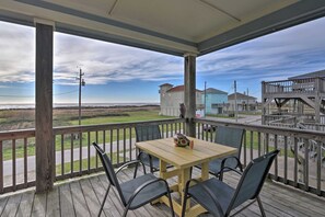 A wooden deck with a table and chairs, overlooking a beach and buildings.
