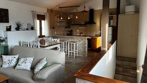 Ein geräumiges Wohnzimmer mit grauem Sofa und Holztisch, eine Küche mit gefliestem Rücksprüher und Pendelleuchten sowie eine Treppe mit Holzwand.