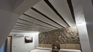 Ein Schlafzimmer mit zwei Betten, einer Steinwand und einer schrägen Decke mit Holzbalken.