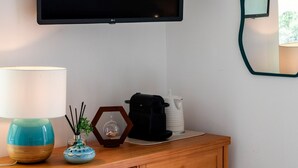 A wooden cabinet with a flat-screen TV mounted above it, a lamp, a small blue vase, and a decorative mirror on the wall. - Room-breathtaking Suite With Sea View in (Positano)