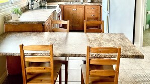 A kitchen with wooden cabinets, a granite countertop, a white refrigerator, and a dining area with wooden chairs. - Stay at Jordan Valley Vineyards Barnhouse (Jordan Station)