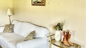 A living room with a sofa, a small table with a vase and boots, and a painting on the wall. - Stay at Jordan Valley Vineyards Barnhouse (Jordan Station)