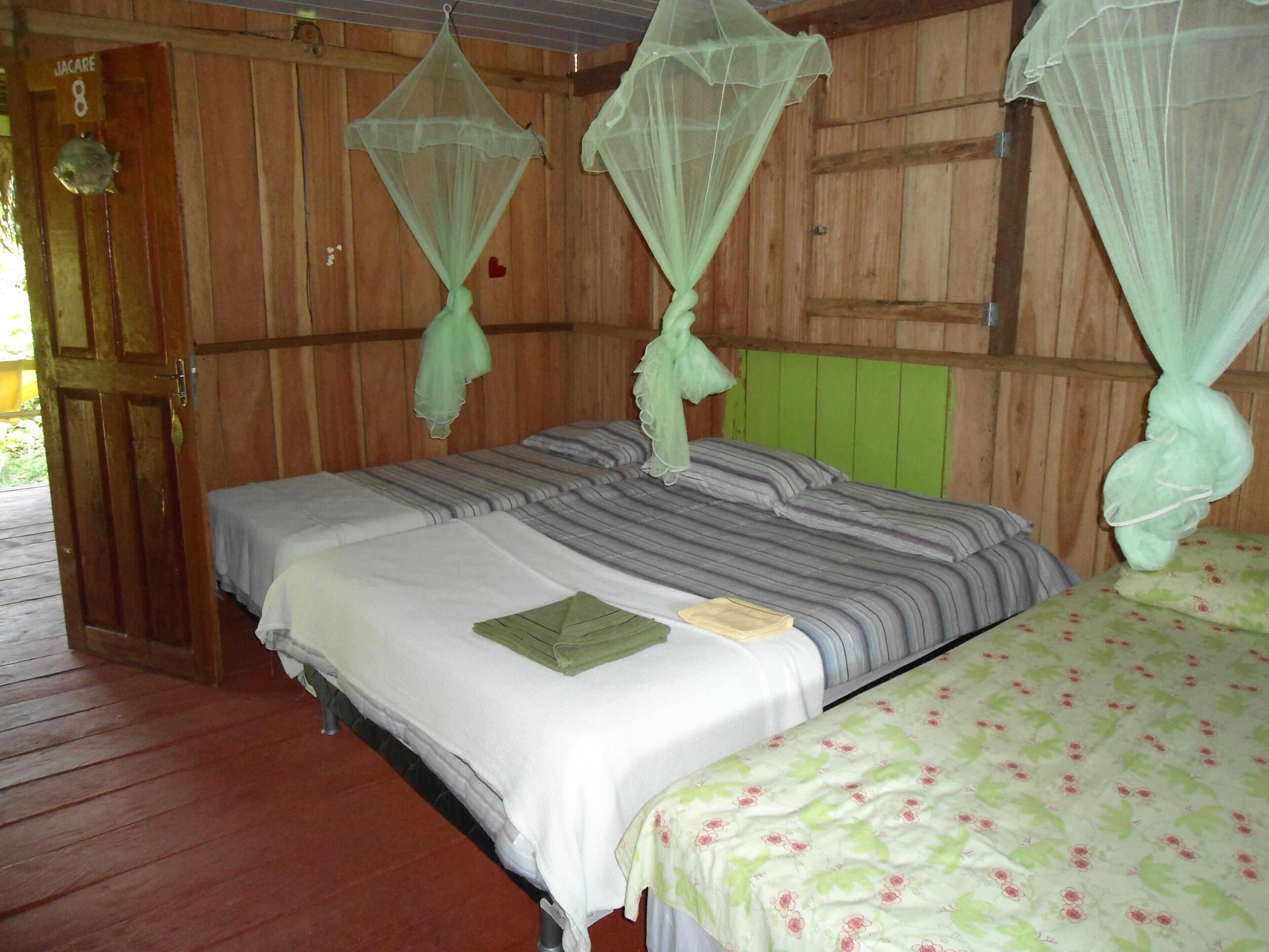 A wooden room with two beds, each with a mosquito net.