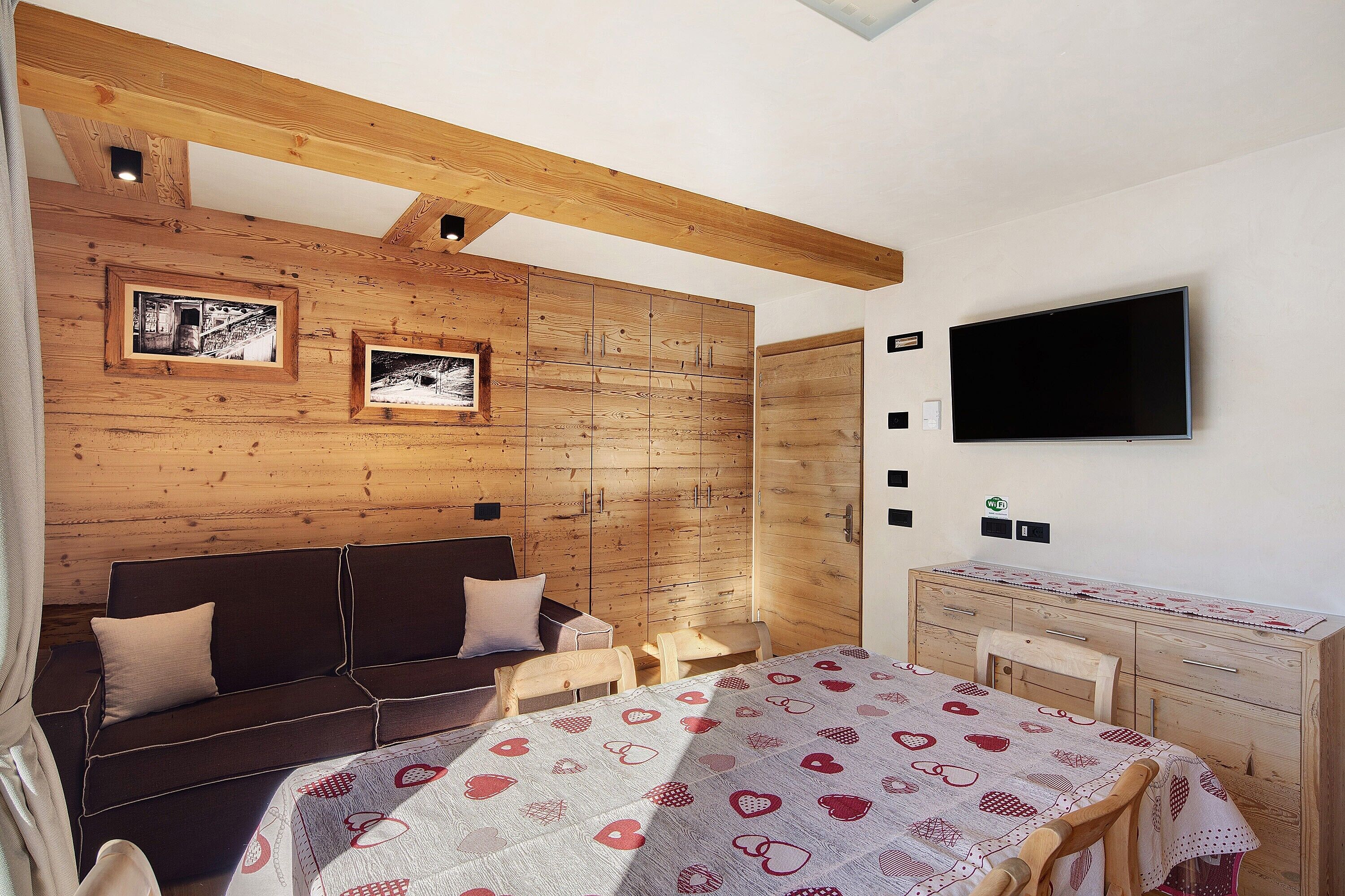 Una habitació amb sostre de fusta, un llit amb mantell estampat, un sofà, un televisor i un taulell de vestir de fusta.