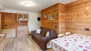 Una habitación acogedora con una pared de madera, un sofá, una mesa con mantel estampado y un aparador con puertas de vidrio.