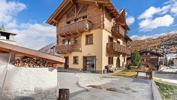 Un edificio de madera de varios pisos, con balcones, fachada de piedra y montañas al fondo.