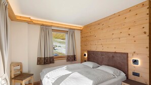 Un dormitorio con cabecera de madera, dos camas, una mesita de noche, una silla y una ventana con cortinas.