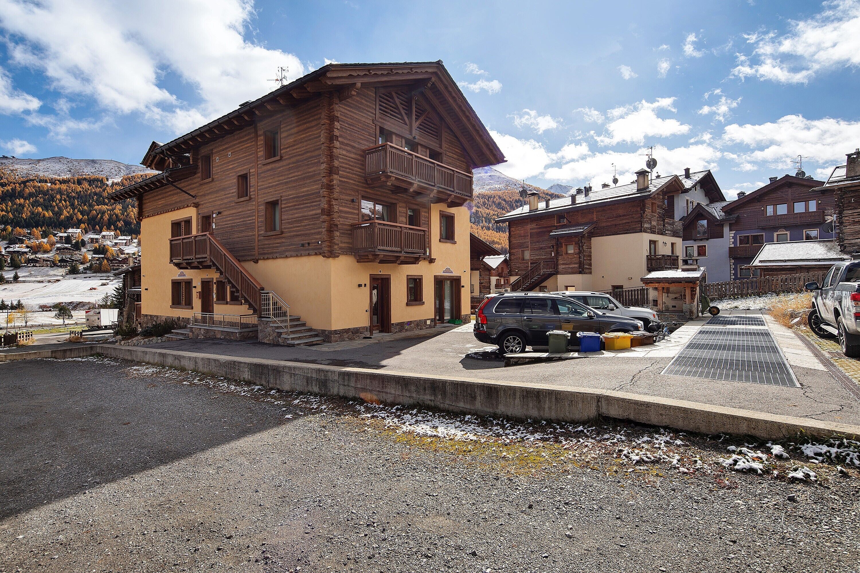 Un bâtiment en bois doté d’un balcon, une voiture garée devant, et une vue sur une région montagneuse.