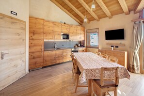 A wooden kitchen with a dining table, chairs, and a TV mounted on the wall. - Apartment 'Larice' with Mountain View, Shared Garden and Wi-Fi (Livigno)