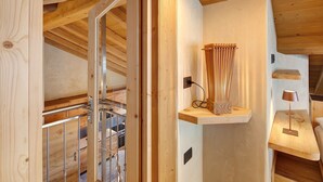 A wooden interior with a staircase, a shelf with a lamp, and a wall-mounted power outlet.