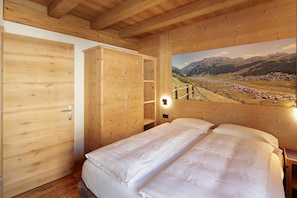 A wooden room with a bed, wardrobe, and a painting of a mountain landscape. - Apartment 'Larice' with Mountain View, Shared Garden and Wi-Fi (Livigno)