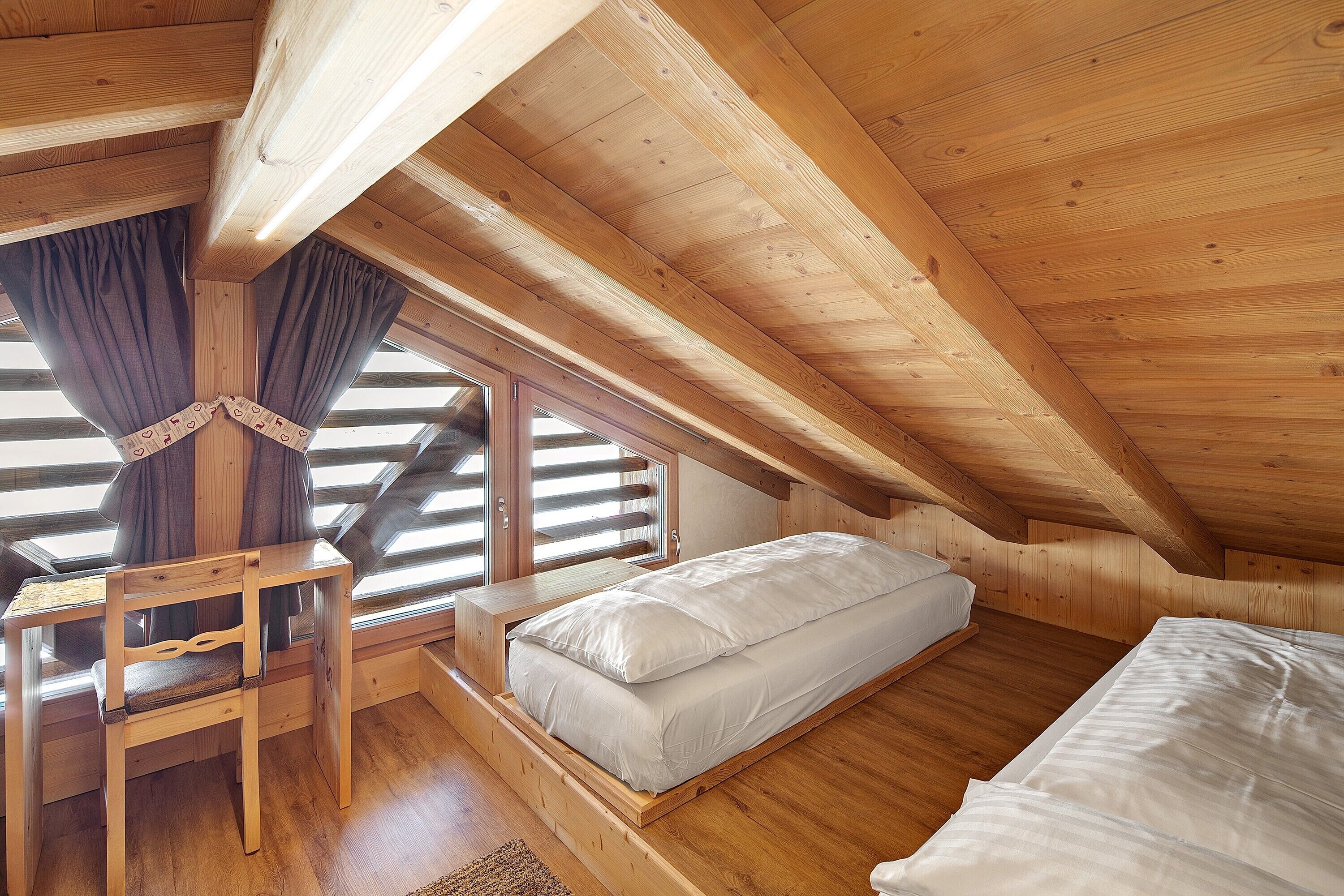 Ein Schlafzimmer im Dachgeschoss mit Holzboden, einem Bett, einem Stuhl und einem Fenster mit Jalousien.