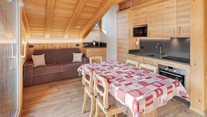 A compact kitchen with wooden cabinets, a dining table with a patterned tablecloth, and a built-in oven. - Apartment 'Rovere' with Mountain View, Shared Garden and Wi-Fi (Livigno)