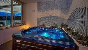 Ein Whirlpool in einem Zimmer mit großem Fenster, einer gefliesten Wand und einigen Pflanzen.