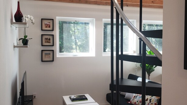 A modern living room with a wooden ceiling, a black spiral staircase, a white sofa, a small table, and a TV.