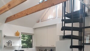 A modern kitchen with white cabinets, a stainless steel dishwasher, and a black staircase.