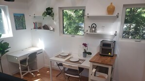A compact kitchen with a dining table, a small oven, and a shelf with kitchenware.