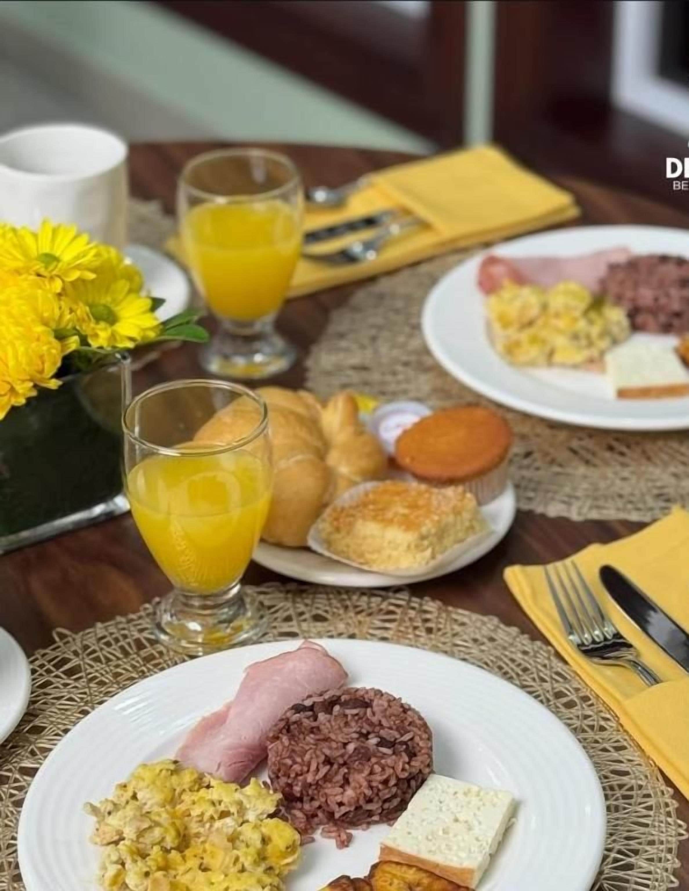 A breakfast setting with plates of food, a glass of orange juice, and a yellow napkin.