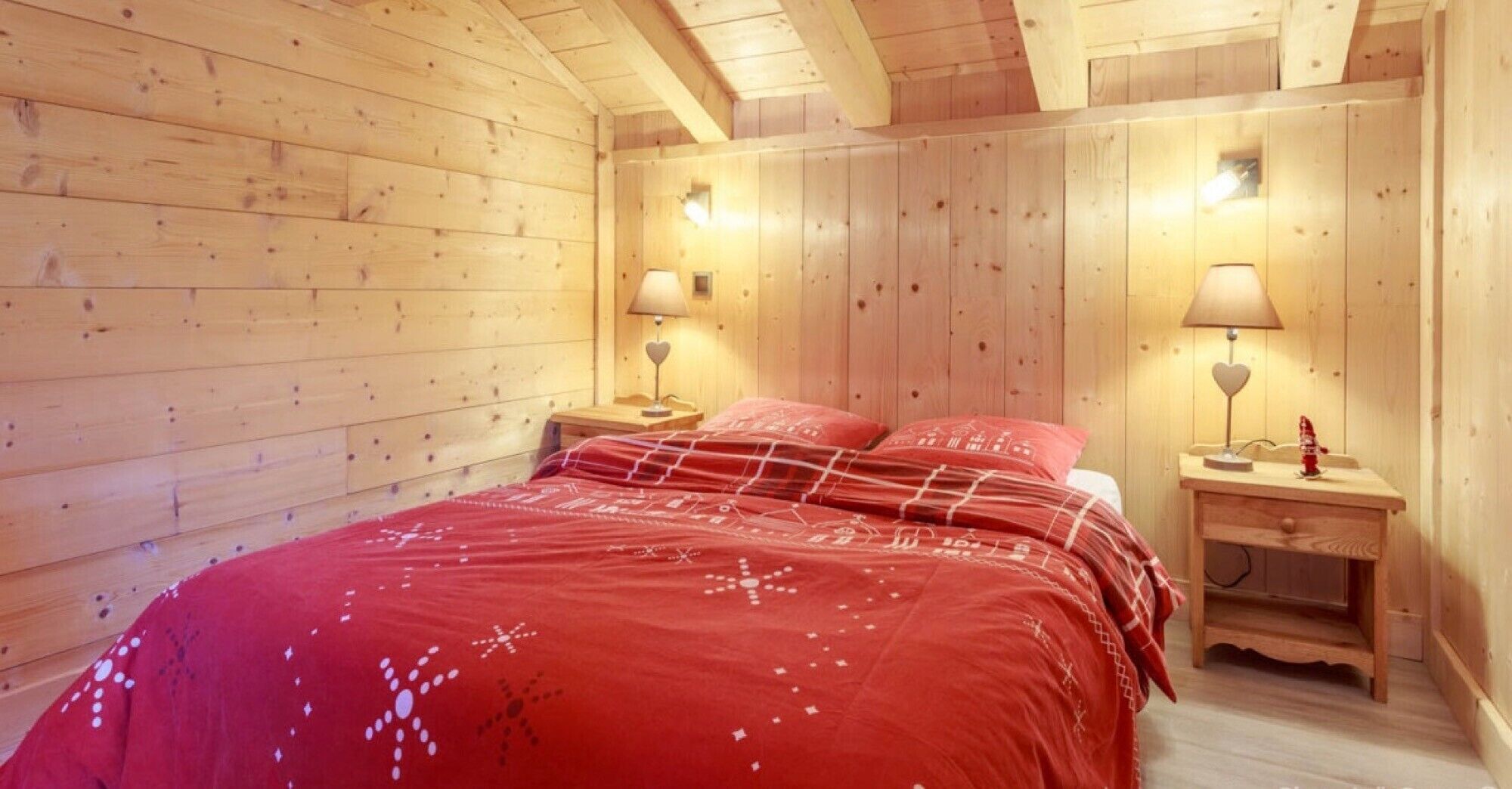 A wooden room with a bed, two bedside tables, and two wall-mounted lamps.