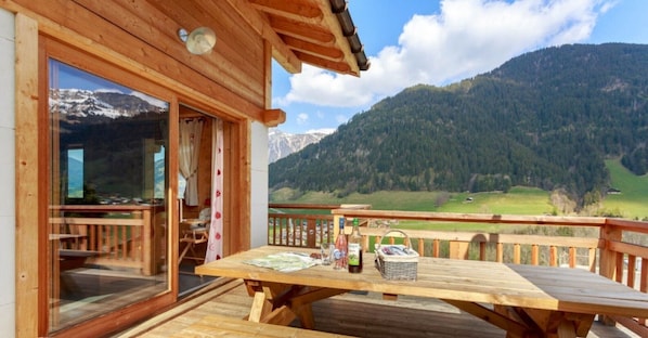 Une terrasse en bois avec une table et des chaises, une bouteille d’alcool et un panier.