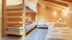 Una cabaña de madera con literas, una mesita con una lámpara y una cama con ropa de cama estampada de animales.