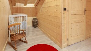 Una habitación de madera con una cuna, una cesta de mimbre y una alfombra roja circular.