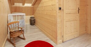 Une pièce en bois avec un berceau, un panier en osier et un tapis rouge circulaire.