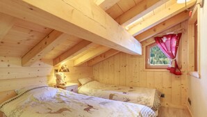 Un dormitorio tipo cabaña de madera con dos camas, una mesita de noche, una lámpara y una ventana con cortina.