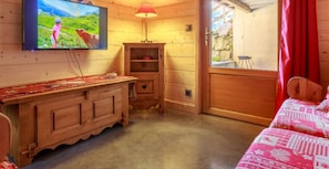 Une pièce de type cabane en bois, équipée d’une télévision, d’une petite armoire, d’un lit et d’une fenêtre avec des rideaux.