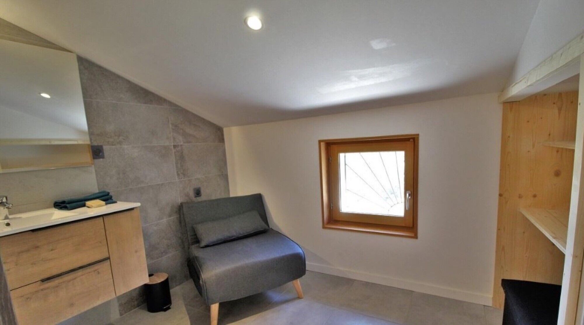A modern bathroom with a grey sofa, a large mirror, and a window.