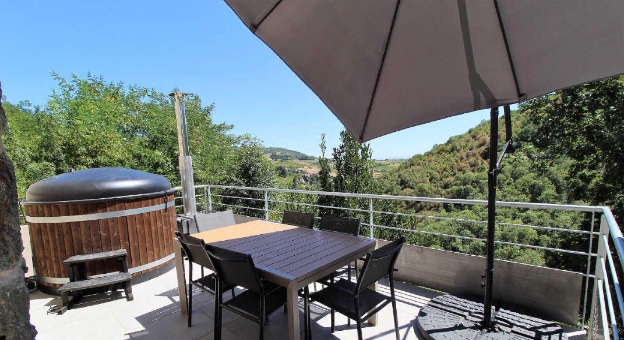Ein Balkon mit Holztisch, Stühlen, einem Whirlpool und Blick ins Grüne.