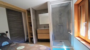 Ein Schlafzimmer mit Bett, integriertem Kleiderschrank, Bad mit Dusche und einem Fenster.