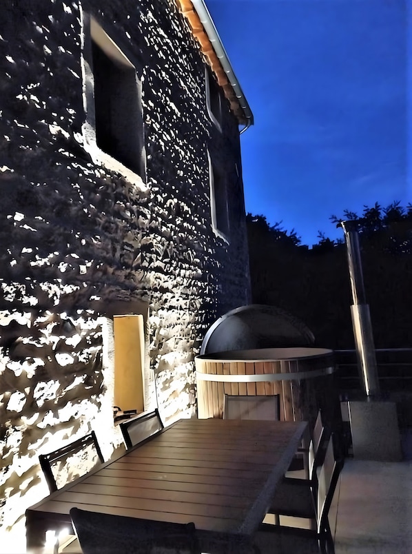 A stone building with a wooden deck, a barbecue grill, and a window.