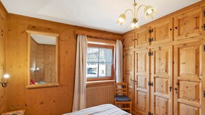 A wooden room with a bed, a chair, a window with curtains, and a mirror. - Apartment 'Di Bernardin' with Mountain View and Wi-Fi (Livigno)