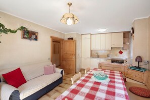 Un espace de vie compact comprenant un canapé, une table à manger, un coin cuisine et une porte donnant sur une autre pièce.