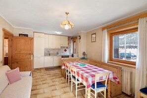 Une cuisine chaleureuse avec des meubles en bois, une table à manger recouverte d’une nappe à carreaux et une fenêtre donnant sur une voiture garée à l’extérieur.