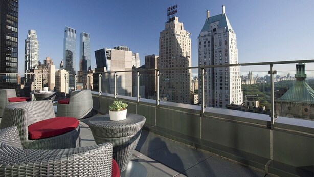 Une terrasse sur le toit, aménagée avec des meubles en osier et agrémentée de plantes en pot, offrant une vue panoramique sur la ville et ses différents bâtiments.