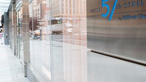 Une façade moderne avec une grande baie vitrée et une enseigne indiquant « West 57th Street by Hilton Club ».