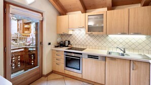Una cocina moderna con armarios de madera, horno empotrado, pileta de acero inoxidable y ventana con vista al exterior.