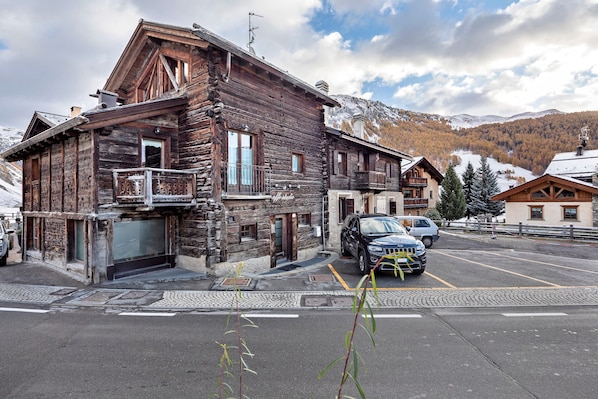 A rustic wooden building with a balcony, a garage, and a parking area.